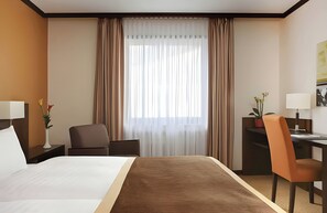 Una habitación de hotel con una cama, un escritorio, una silla y un ventanal con cortinas.