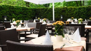 An outdoor dining area with tables set for two, surrounded by greenery. - Steigenberger Hotel Dortmund (Dortmund)
