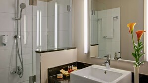 A modern bathroom with a glass-enclosed shower, a white sink, and a vase with flowers. - Leonardo Royal Hotel Dortmund (Dortmund)