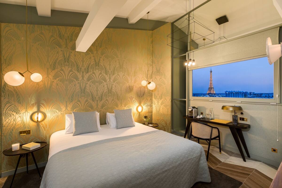 A hotel room with a large bed, a desk, and a view of the Eiffel Tower.