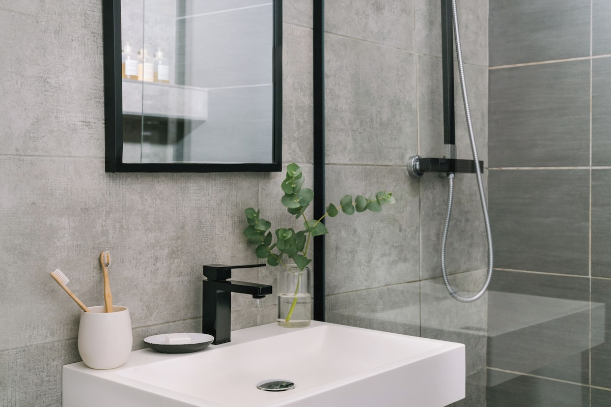 Une salle de bain avec un lavabo blanc, un robinet noir et un vase en verre contenant une plante.