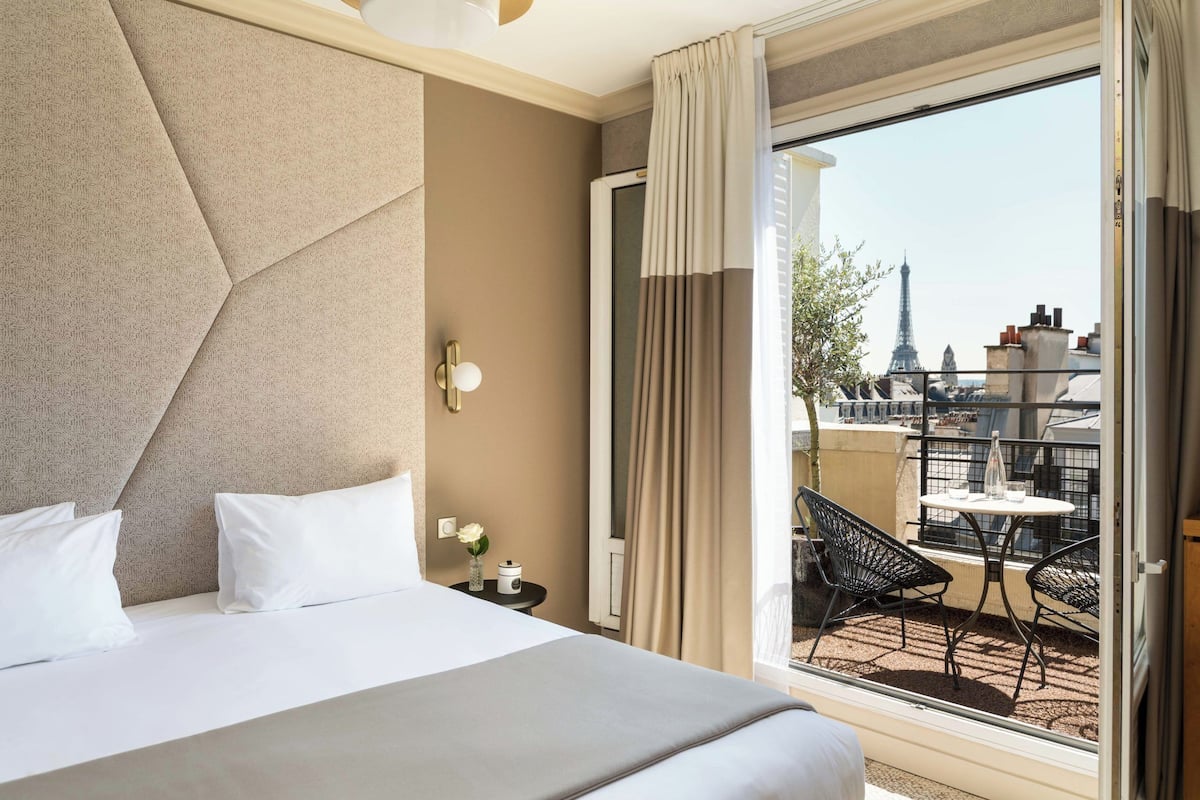 A hotel room with a large bed, a view of the Eiffel Tower, and a balcony with outdoor seating.