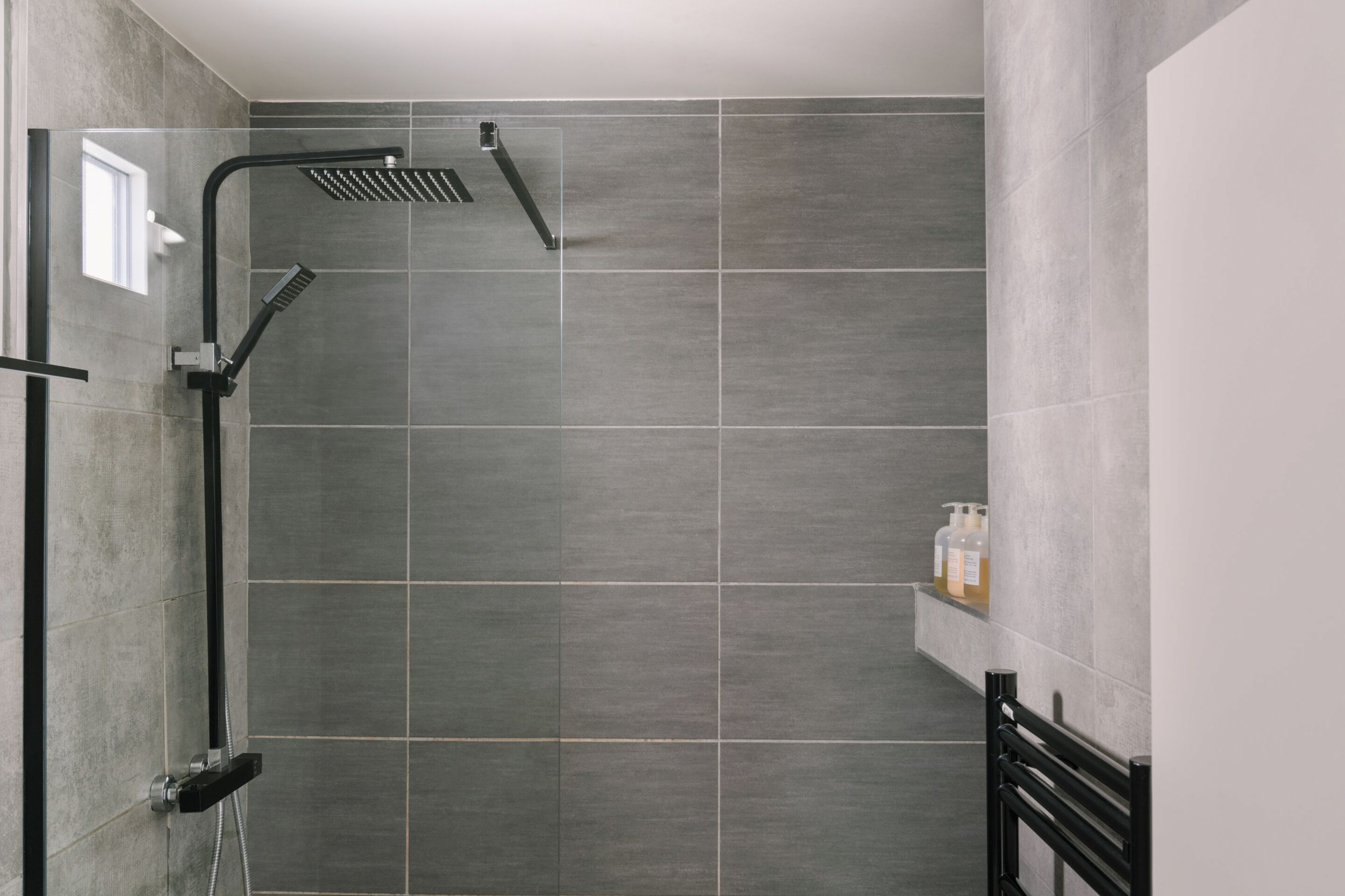 Un área de ducha moderna con cabina de vidrio, azulejos grises y un grifo negro.