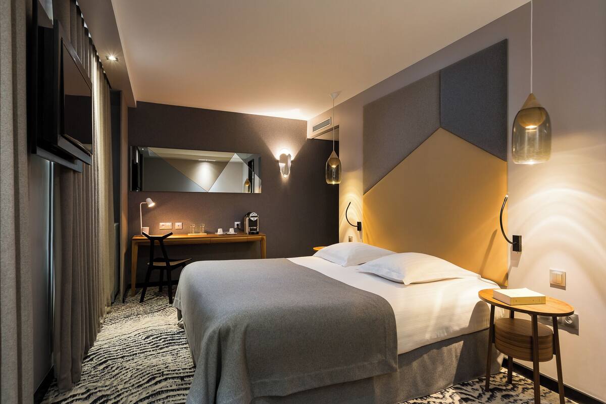 A modern hotel room with a large bed, a desk, and a mirror.