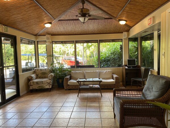 A spacious indoor area with tiled flooring, wicker furniture, and large windows offering views of the outdoors.