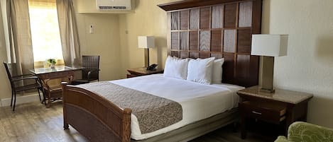 A hotel room with a large bed, a desk, a chair, a ceiling fan, and an air conditioning unit.