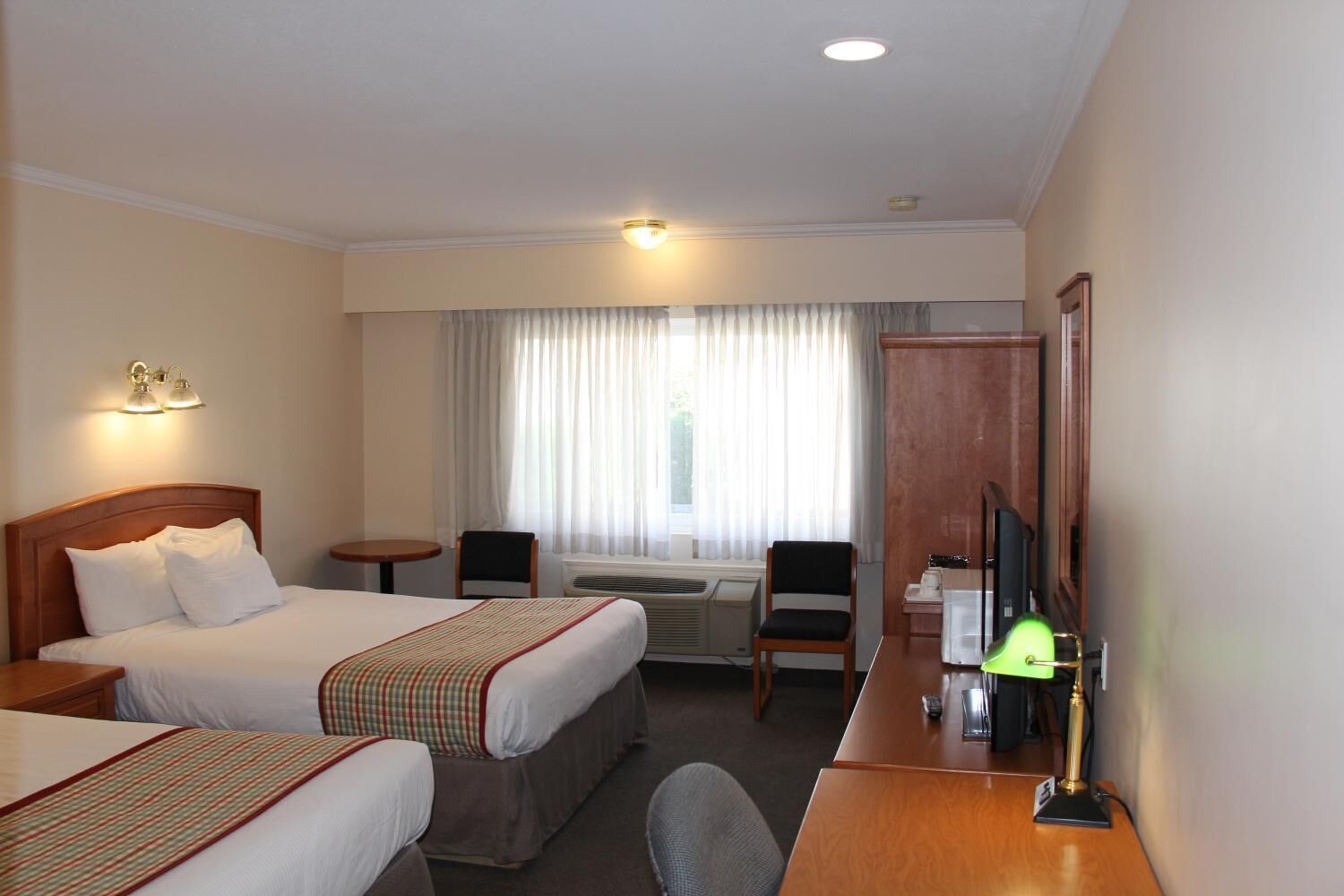 A hotel room with two beds, a desk, a chair, a television, and a window with curtains.
