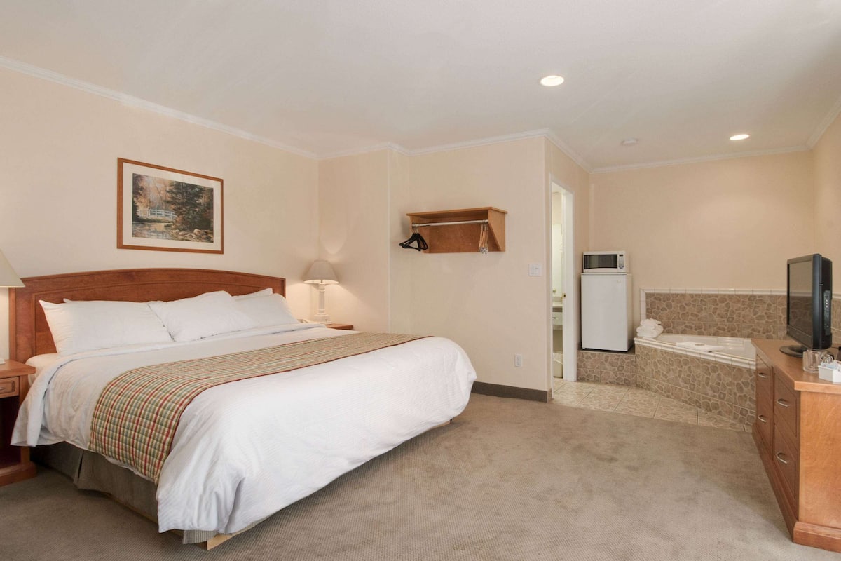 A hotel room with a bed, a nightstand, a lamp, a TV, a microwave, a bathroom with a bathtub, and a towel rack.