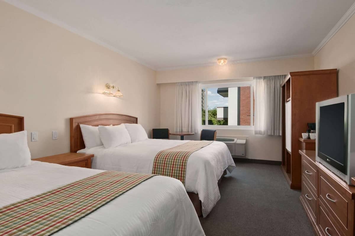 A hotel room with two beds, a desk, a television, and a window with curtains.