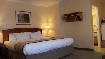A hotel room with a large bed, a nightstand, a lamp, a framed picture on the wall, and a coat rack.