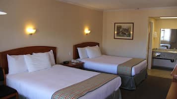 A hotel room with two beds, a bathroom with a sink, and a painting on the wall.
