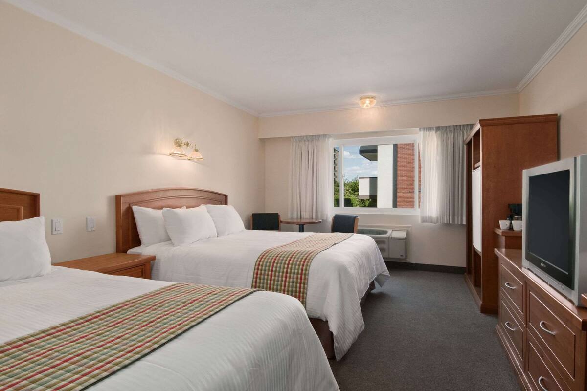 A hotel room with two beds, a desk, a television, and a window with curtains.