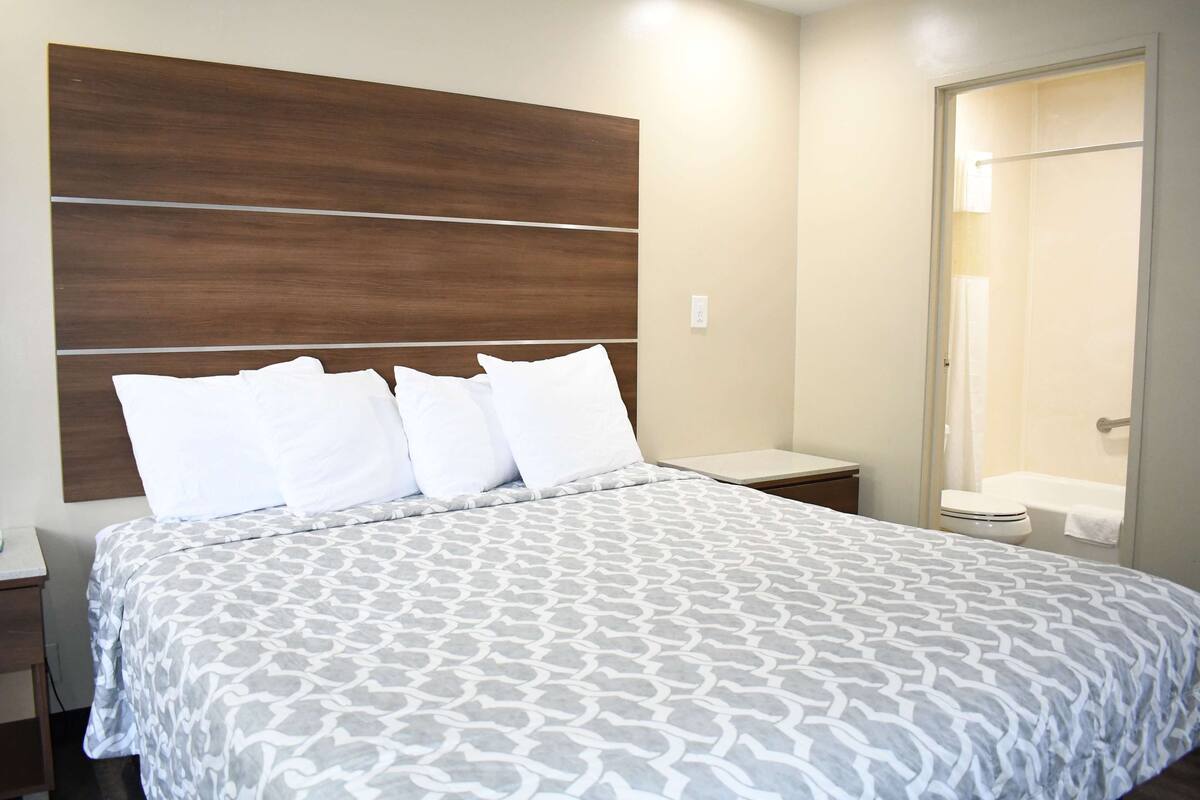 Een hotelkamer met een groot bed, een houten hoofdeinde, een nachtkastje en een zichtbare badkamer door een open deur.