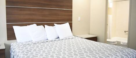 A hotel room with a large bed, a wooden headboard, a bedside table, and a bathroom visible through an open door.