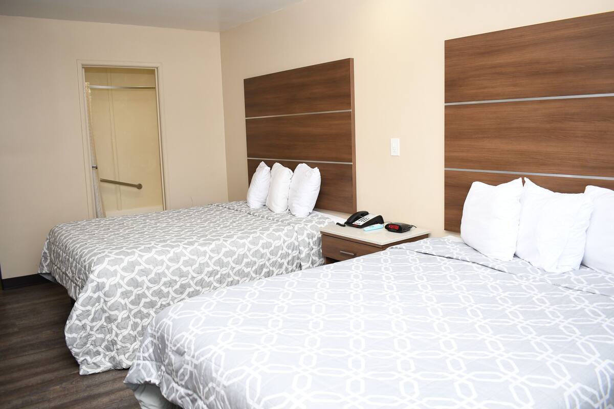 Een hotelkamer met twee bedden, een houten hoofdbord, een nachtkastje met een telefoon, en een deur.