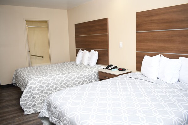 Una habitación de hotel con dos camas, un cabecero de madera, una mesita de noche con un teléfono y una puerta.
