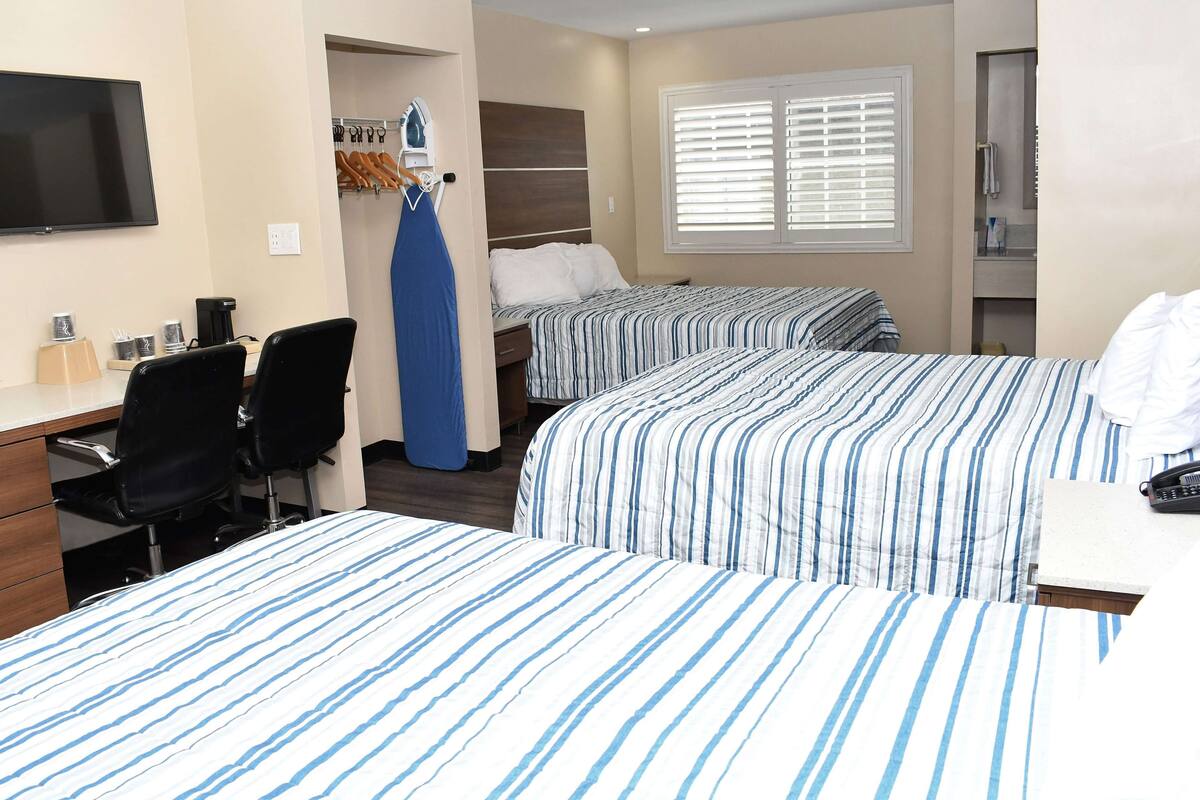 Hotelkamer met twee bedden, een bureau, een stoel, een televisie en een raam met jaloezieën.