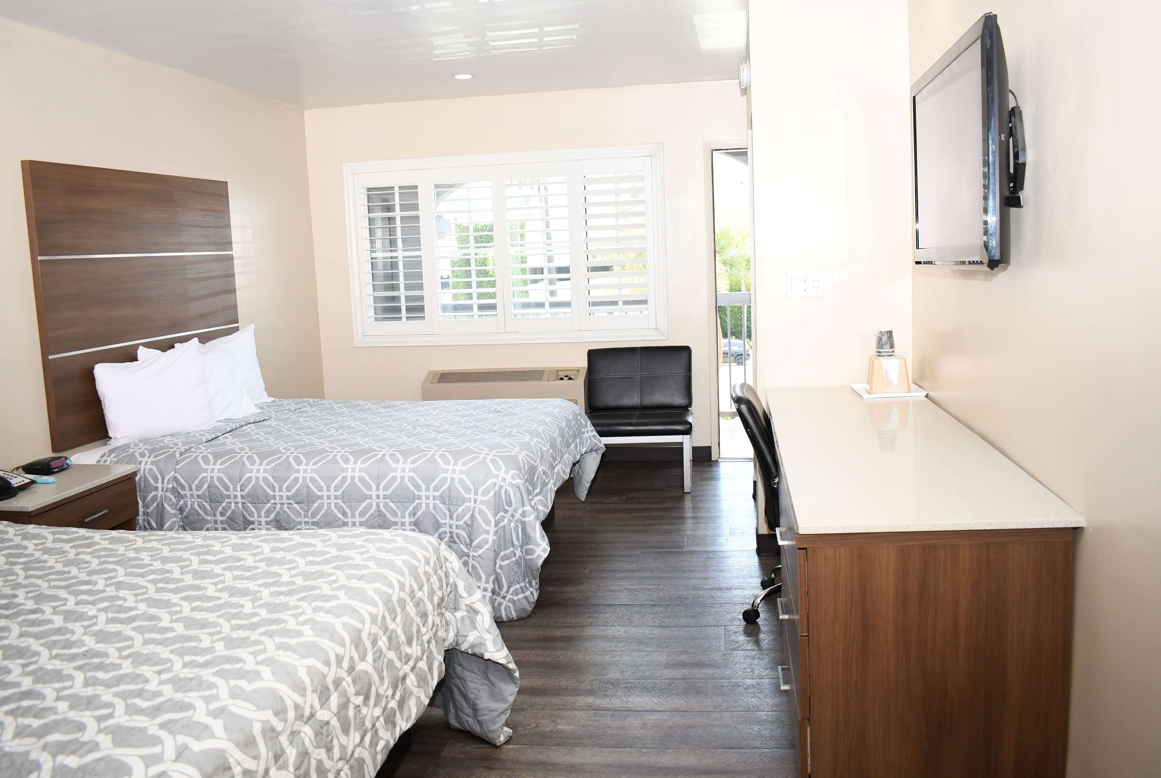 A hotel room with two beds, a desk, a chair, a TV, and a window with blinds.