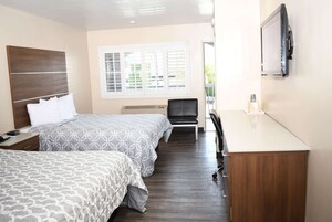 Habitación de hotel con dos camas, un escritorio, una silla, un televisor y una ventana con persianas.