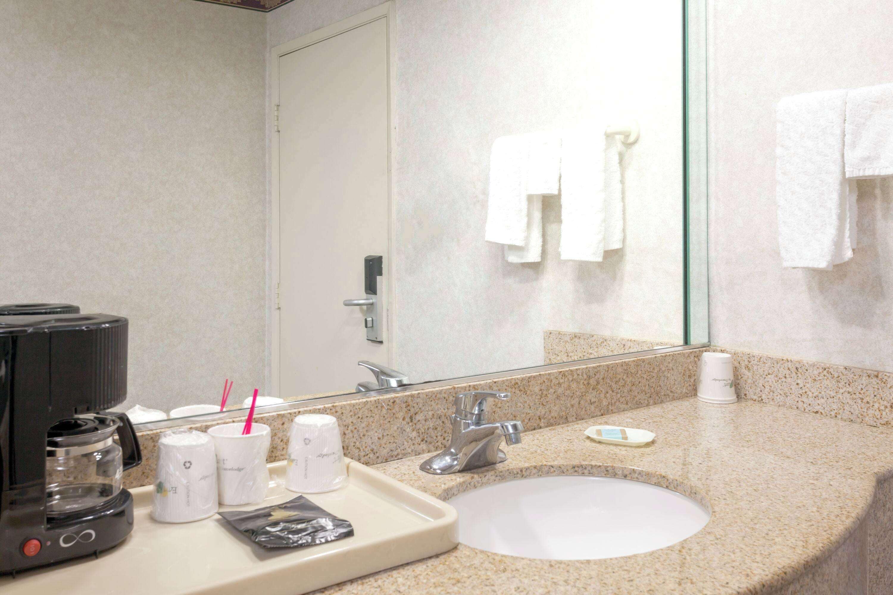A hotel bathroom with a sink, mirror, and coffee maker.