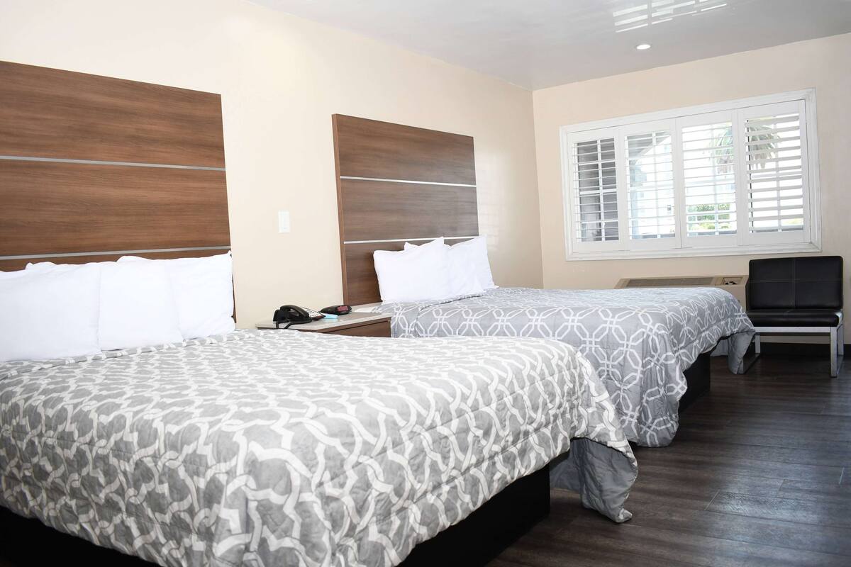 Een hotelkamer met twee bedden, houten hoofdeinden, een raam met zonwering, een bureau en een stoel.