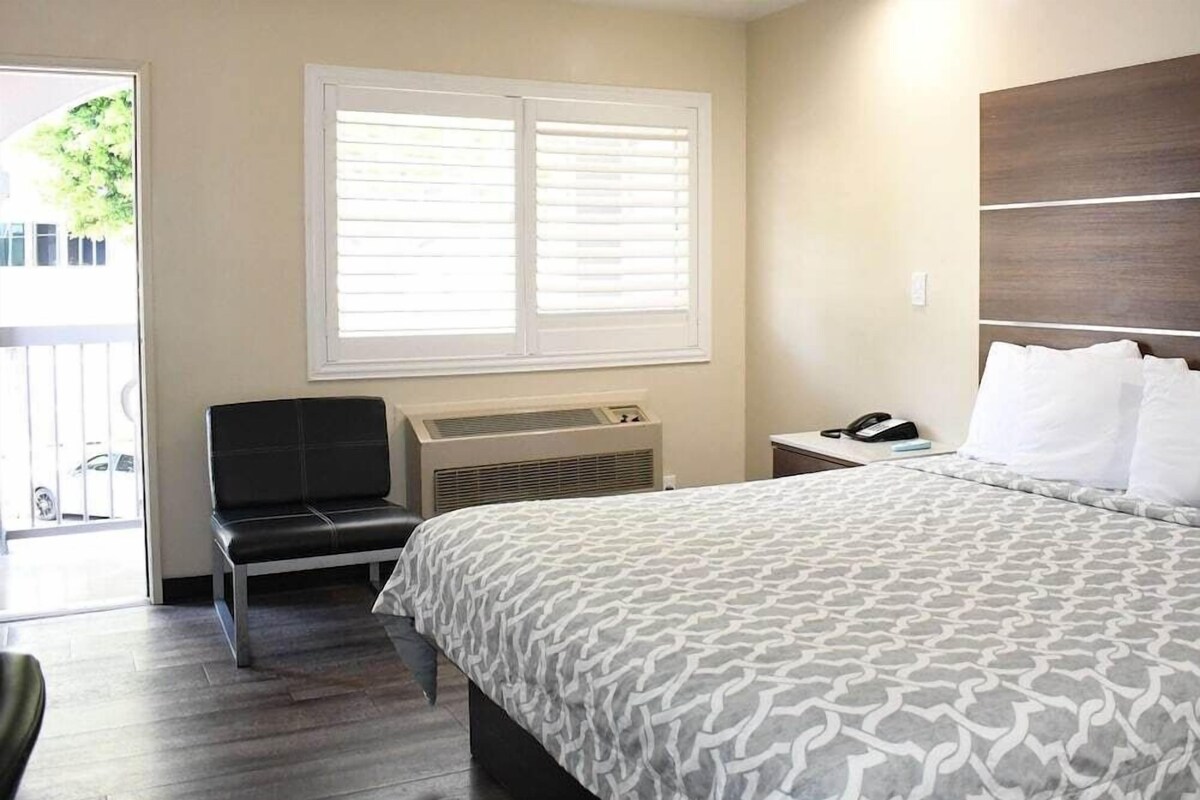 Habitación de hotel con cama, una silla, mesita de noche con teléfono y ventana con persianas.