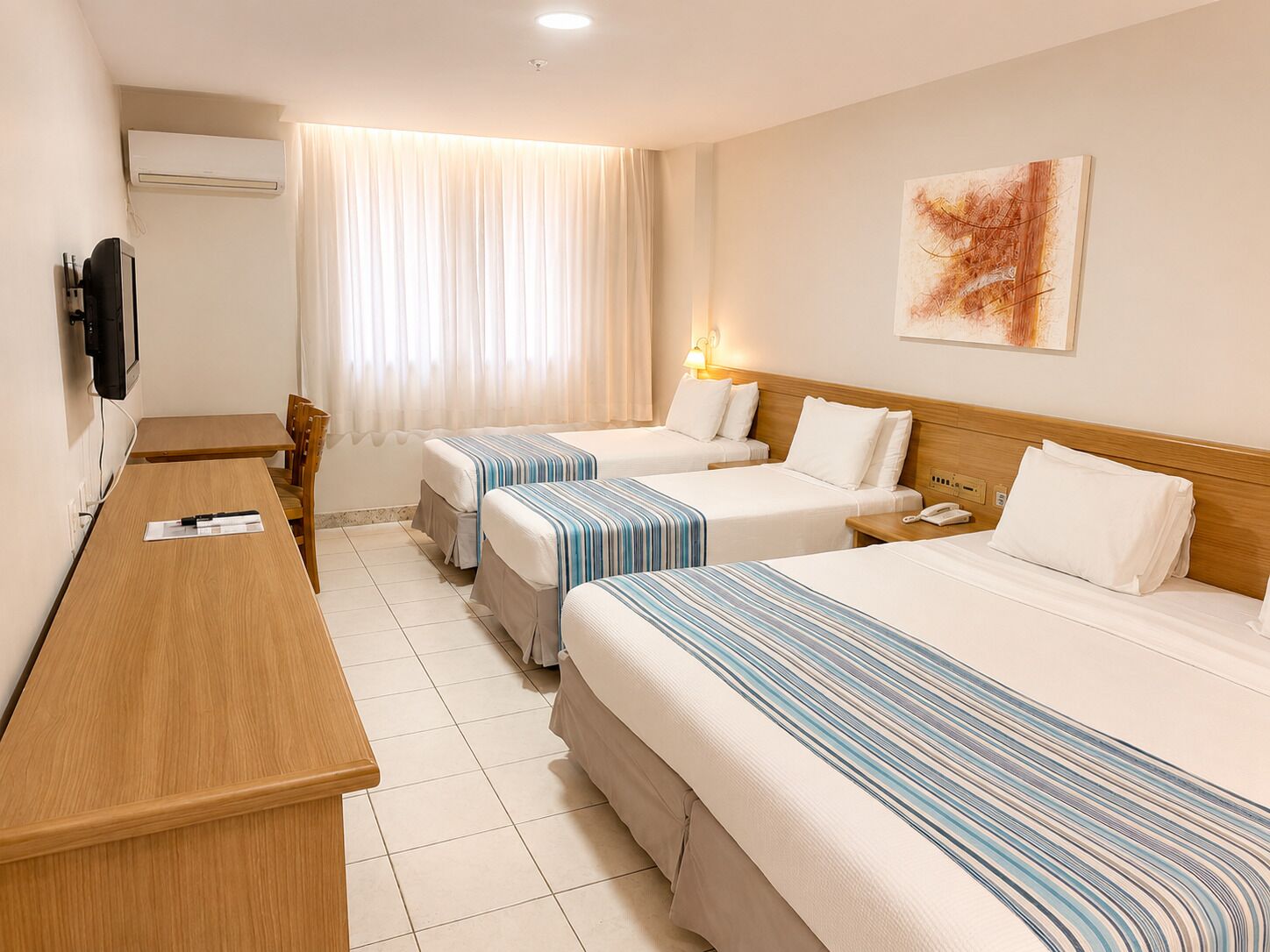 A hotel room with two beds, a desk, a TV, and a window with curtains.
