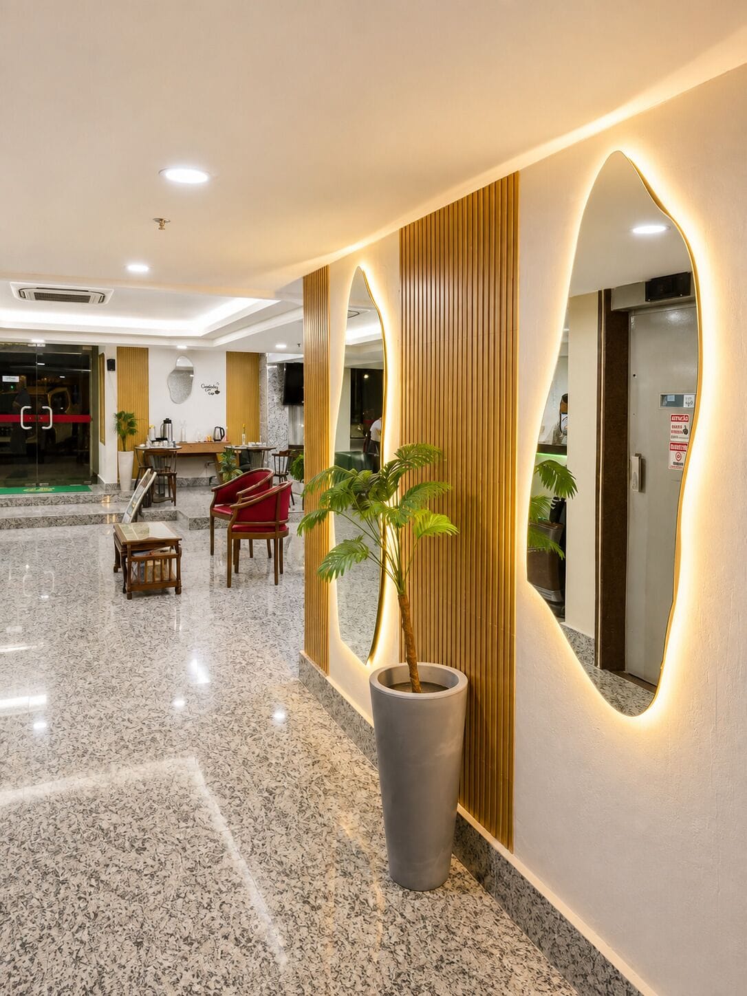 Um hall de hotel com uma mesa de recepção, área de estar e uma grande planta em vaso.