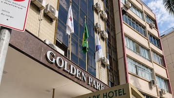 Exterior do Hotel Golden Park, com entrada visível, placa proibindo estacionamento e diversas bandeiras.