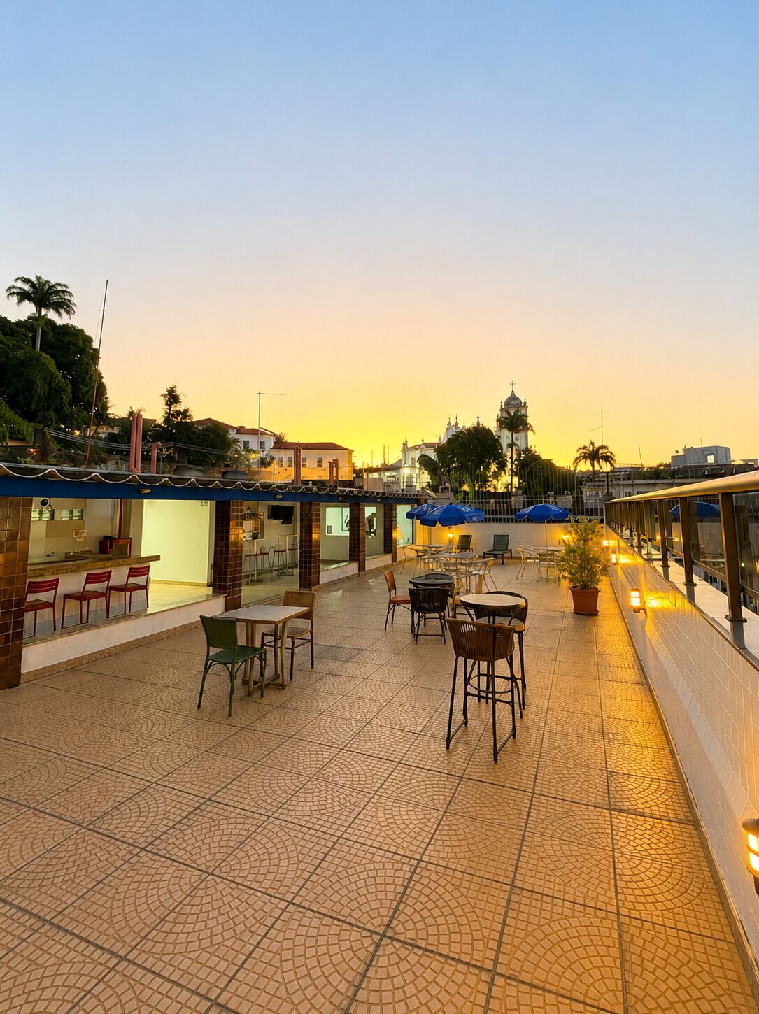 An outdoor café area with tables and chairs, a tiled floor, and a view of a building with a dome in the background.