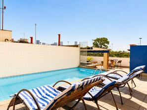 A rooftop pool area with lounge chairs and a table, surrounded by a high wall and a clear sky. - Hotel Golden Park Rio de Janeiro Aeroporto By Nacional Inn (Rio de Janeiro)