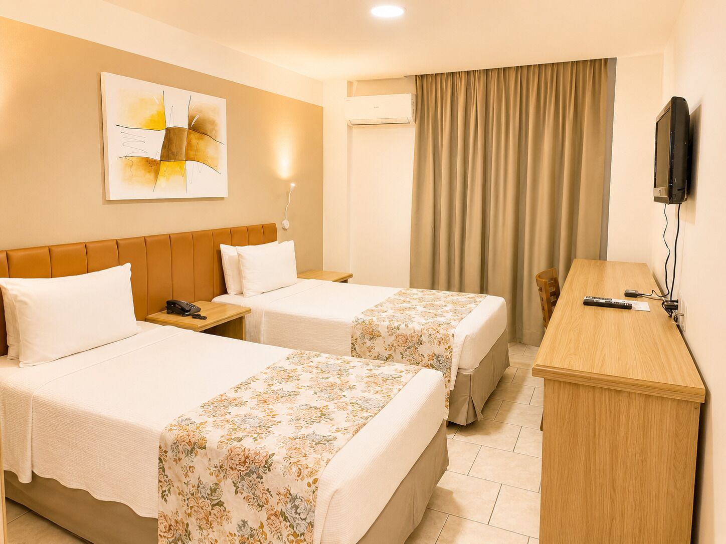 Ein Hotelzimmer mit zwei Betten, einem Schreibtisch, einem Fernseher und einem Bild an der Wand.