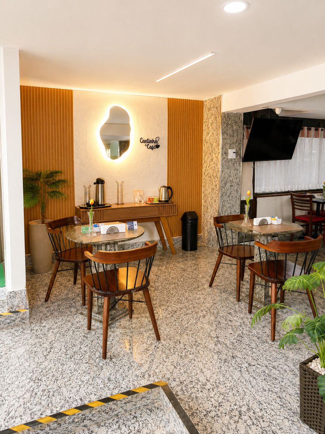 Um café com uma mesa redonda, cadeiras, uma máquina de café e um espelho fixado na parede.