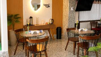 Um café com uma mesa redonda, cadeiras, uma máquina de café e um espelho fixado na parede.