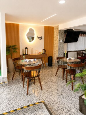 A cafe with a round table, chairs, a coffee machine, and a wall-mounted mirror. - Hotel Golden Park Rio de Janeiro Aeroporto By Nacional Inn (Rio de Janeiro)