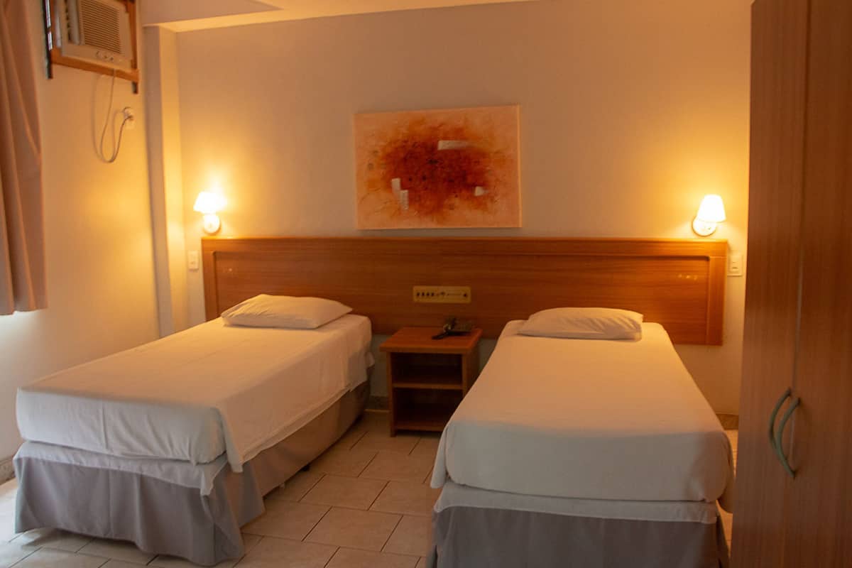 Habitación de hotel con dos camas individuales, cabecero de madera, mesita de noche y una obra de arte colgada en la pared.