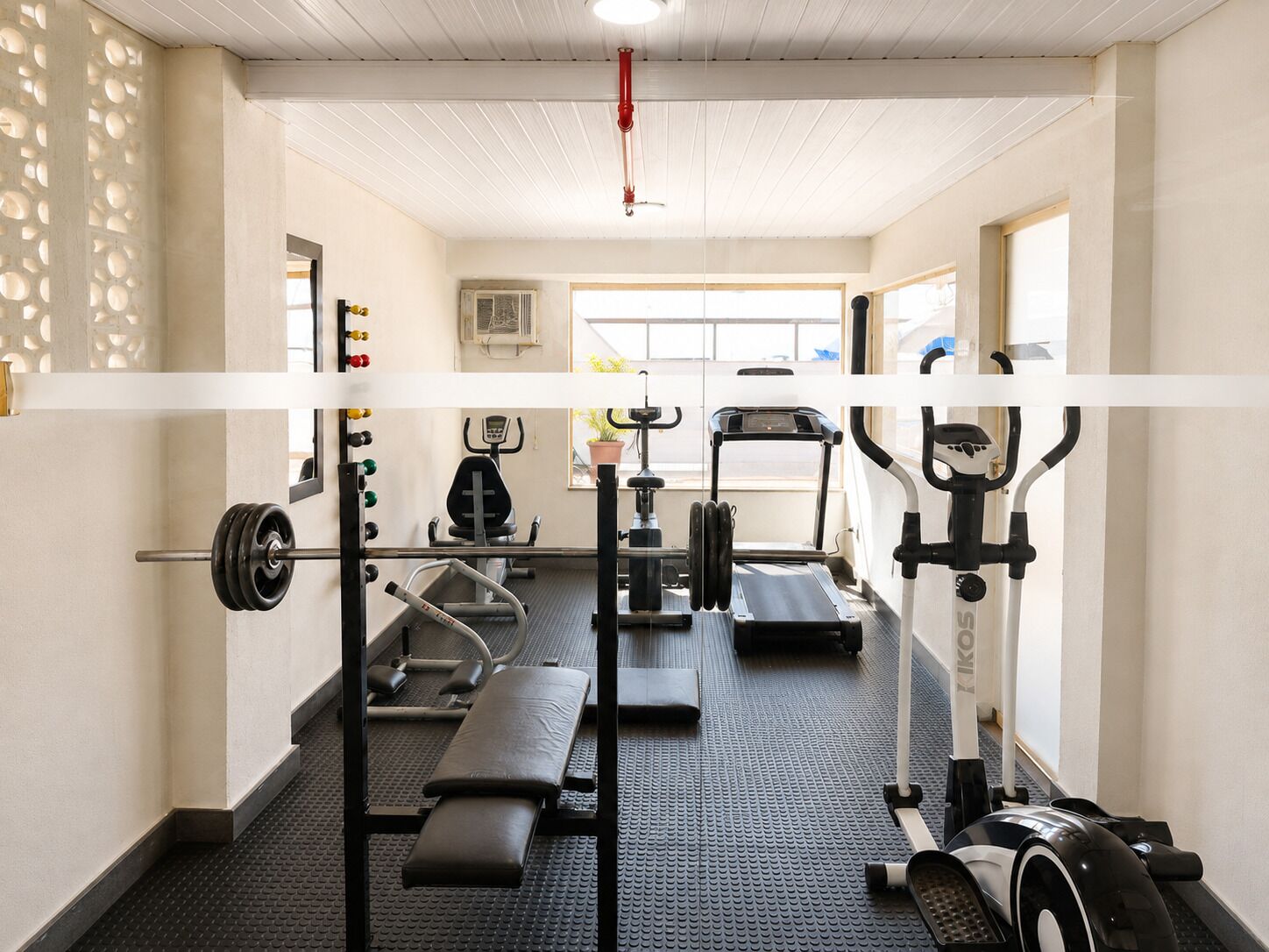 Uma academia com diversos equipamentos de exercício, incluindo esteira, elíptico e banco de musculação.