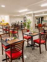 A hotel dining area with multiple tables and chairs, a reception desk, and a potted plant.