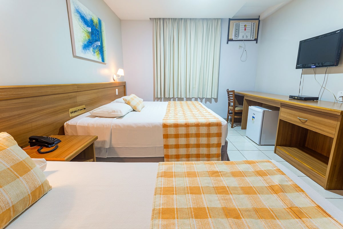 Una habitación de hotel con dos camas, un escritorio, una silla, un televisor y un refrigerador pequeño.