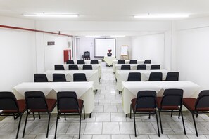 Een vergaderruimte met meerdere tafels en stoelen, een projectiescherm en een whiteboard.