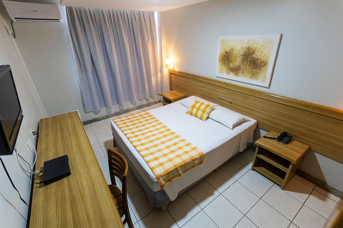 Habitación de hotel con cama, mesitas de noche, escritorio, silla, televisor y aire acondicionado.