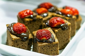 Een wit rechthoekig bord met verschillende vierkante stukken cake, belegd met aardbeien en chocolade.