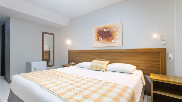 Habitación de hotel con una cama grande, cabecera de madera, mesita de noche, escritorio, silla, espejo y una obra de arte colgada en la pared.
