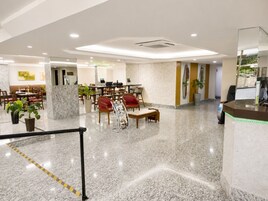 Um saguão de hotel com piso de mármore, áreas de estar, balcão de recepção e uma prancha de surf fixada na parede.