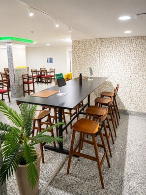 Uma sala de conferências com uma mesa comprida, várias cadeiras, um vaso de planta e uma parede com padrão de pedra.