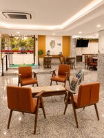Um hall de hotel com área de estar, balcão de recepção e uma tela de televisão.