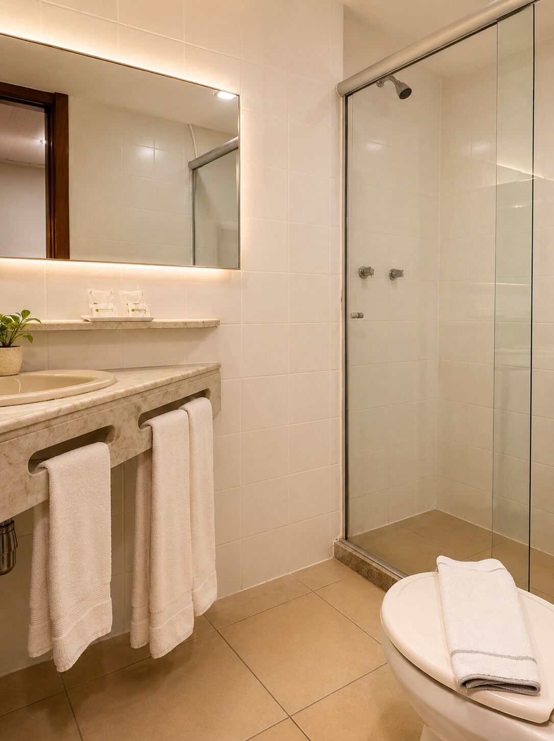 Uma casa de banho moderna com cabine de duche em vidro, lavatório com espelho e sanita.