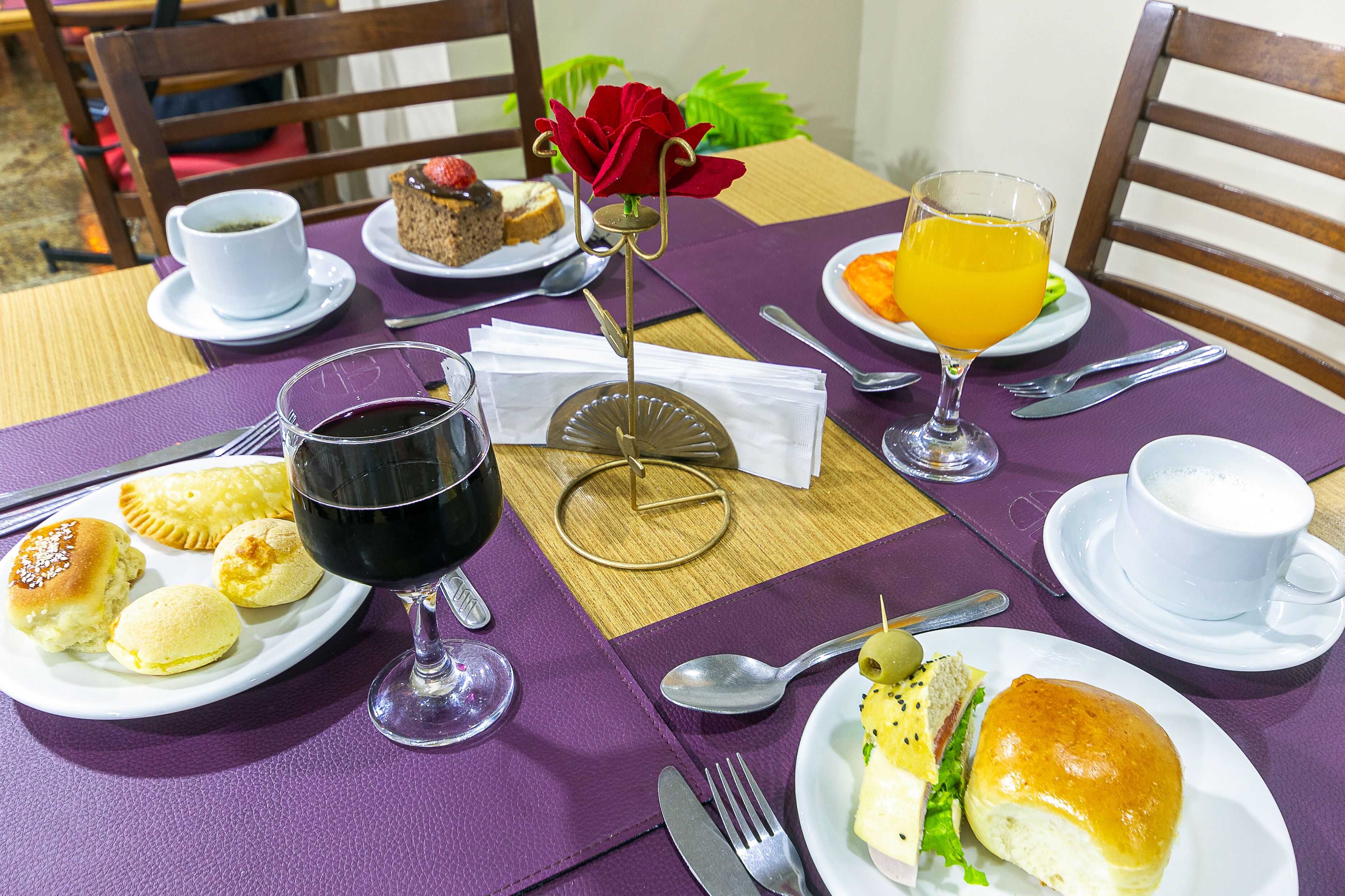 A table set with plates of pastries, a glass of red wine, a glass of orange juice, and a cup of coffee.