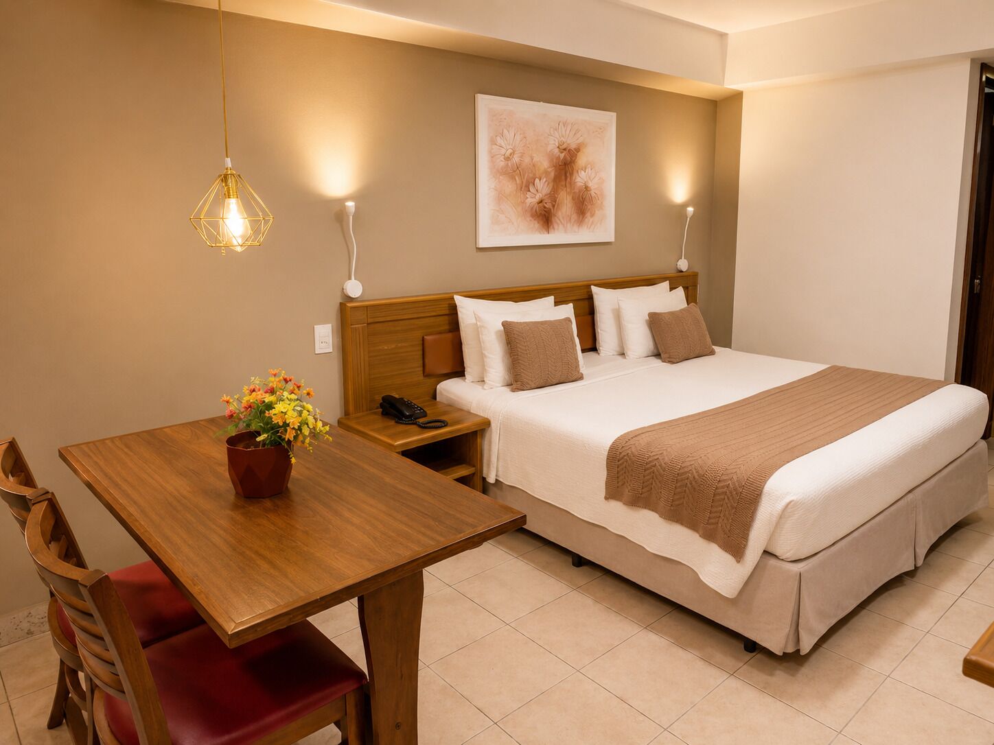 Een hotelkamer met een bed, nachtkastje, stoel en een aan de muur hangend kunstwerk.