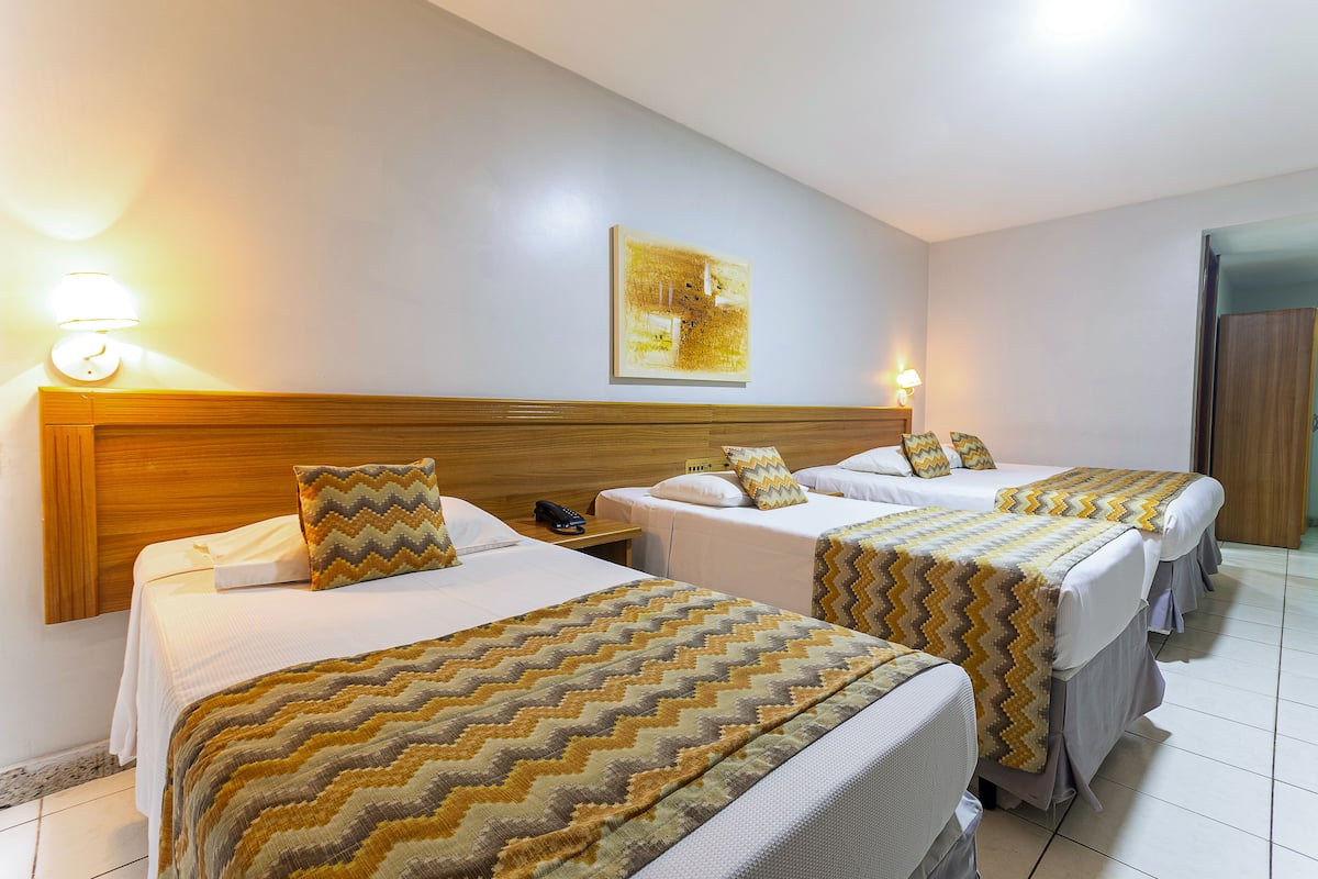 Habitación de hotel con tres camas, cada una con una colcha estampada, cabecero de madera y lámparas de noche.